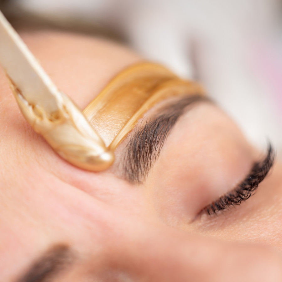 Applying Gold Colored Wax with Spatula on Woman's Face - stock photo